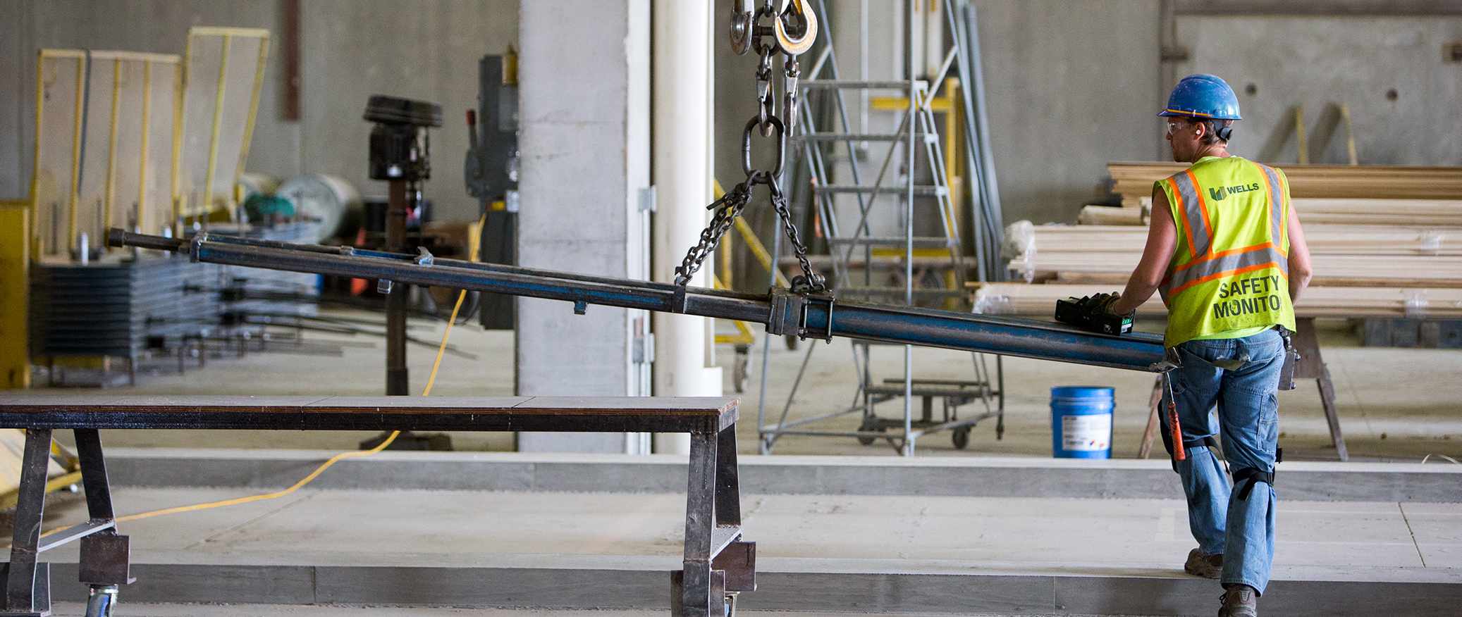 Worker in yellow safety vest and orange helmet next to hanging beam