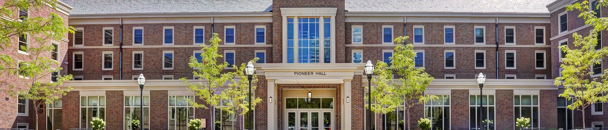 Front view of Pioneer Hall dormitory with greenery framing red brick and windows