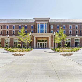 Front view of Pioneer Hall dormitory with greenery framing red brick and windows
