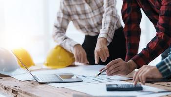 engineers collaborating over a blueprint with computer