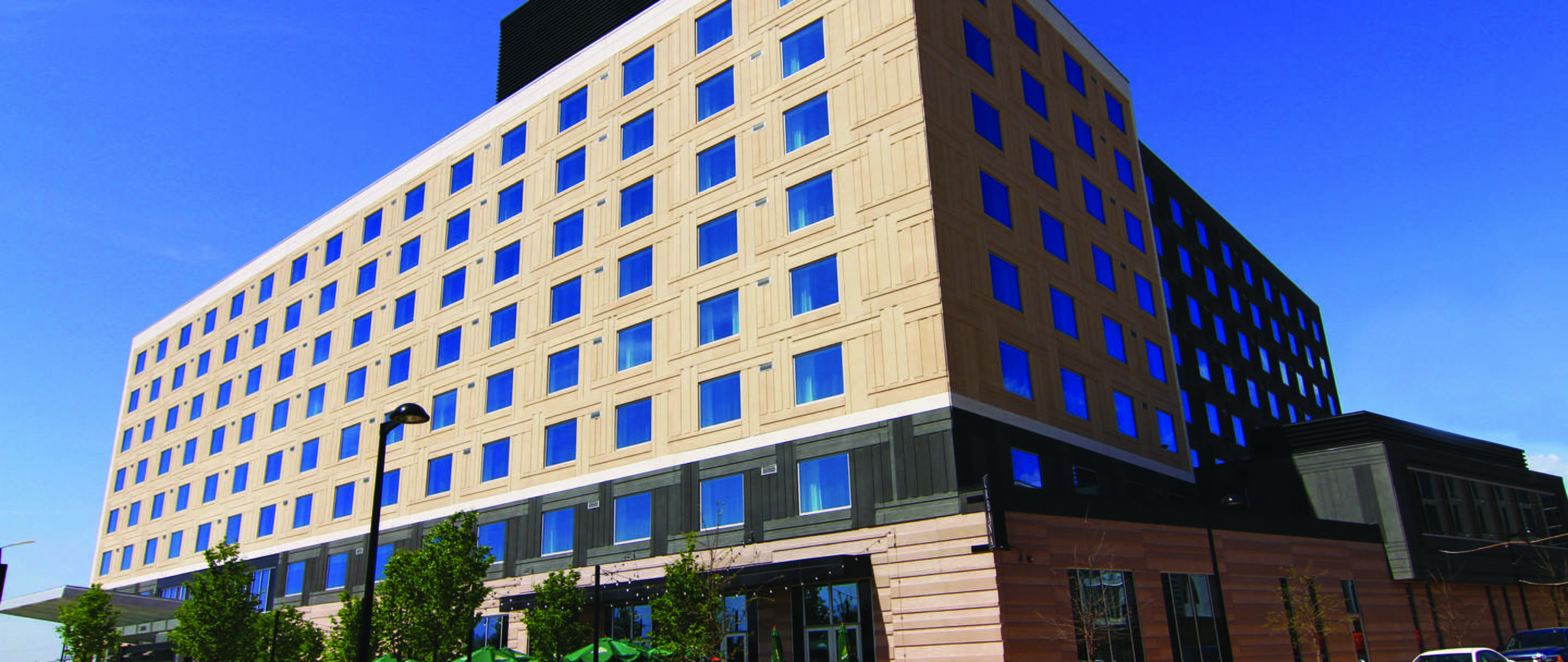 Exterior of BCS Hotel in MN (modular architectural panels with two tone precast finish with windows) with sidewalks, trees and blue sky in back