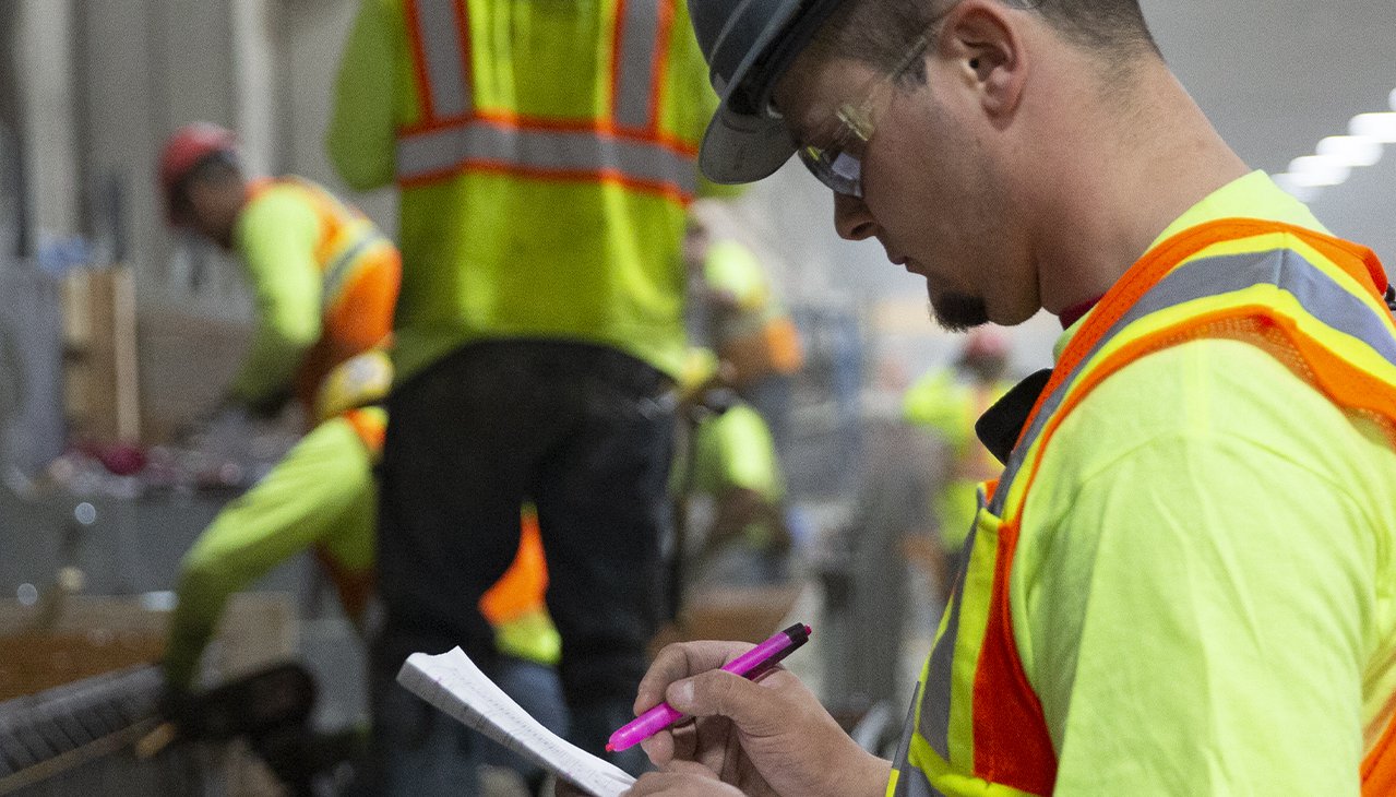 Employees in yellow safety gear and helmets working inside facility reviewing checklist