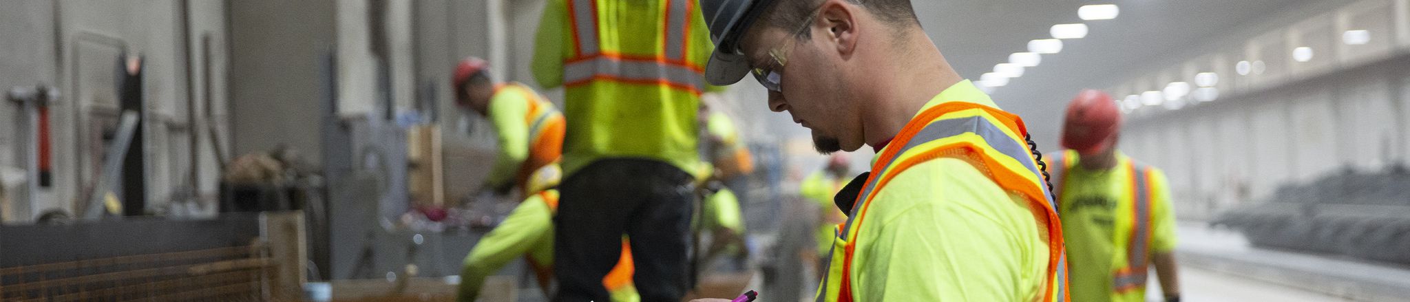 Employees in yellow safety gear and helmets working inside facility reviewing checklist