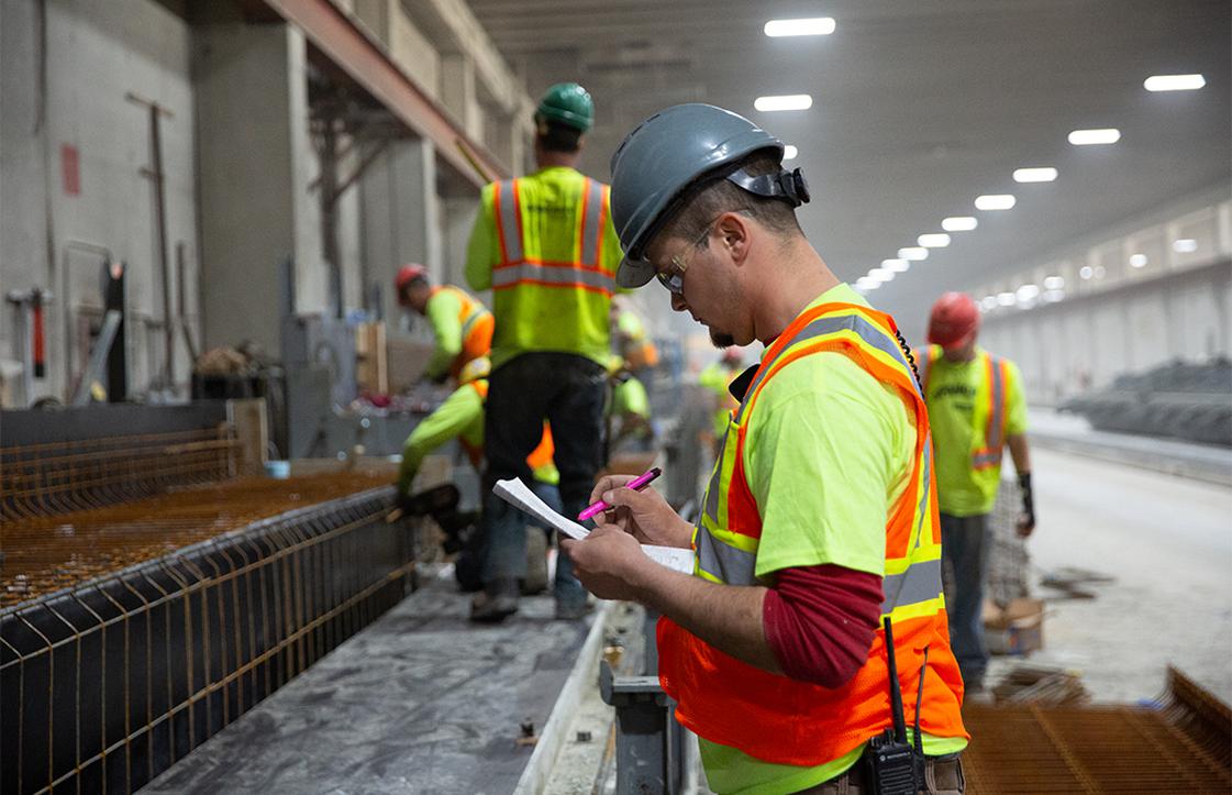 Workers in Yellow safety vests and helmets inside facility reviewing checklist
