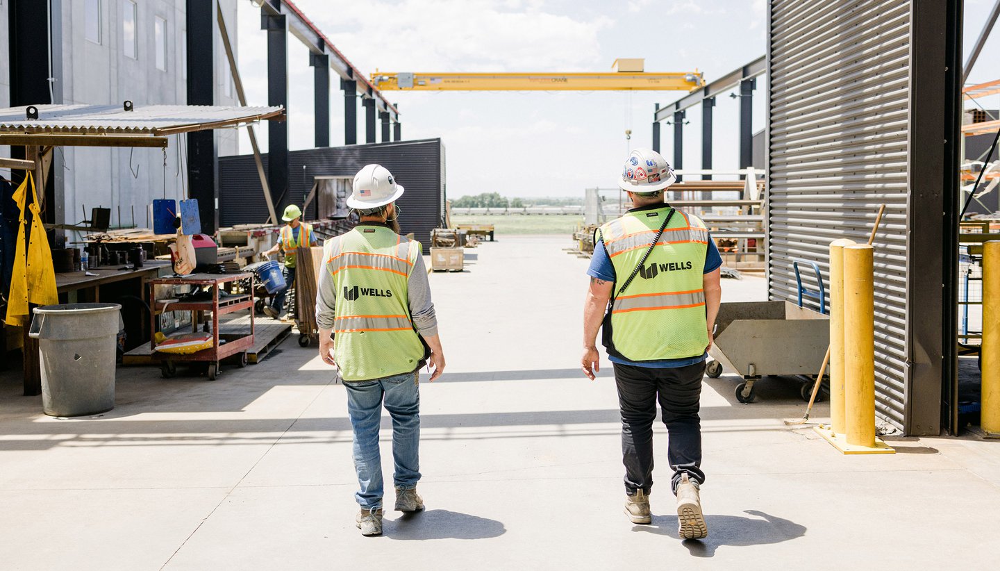Employees in yellow safety gear and helmets working inside facility reviewing checklist
