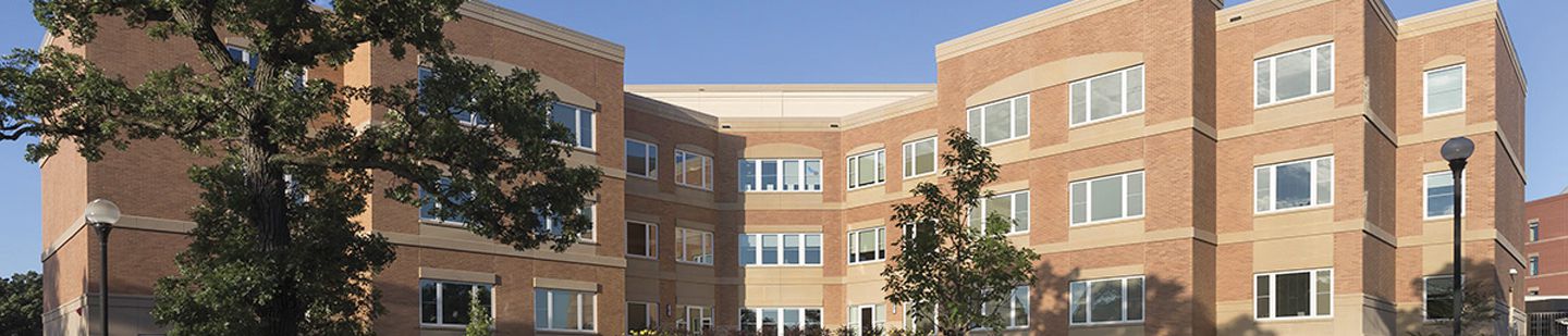 Wide view of Minnesota Veterans home with trees in the foreground and a blue sky.