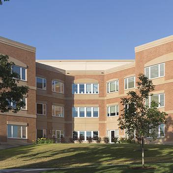 Wide view of Minnesota Veterans home with trees in the foreground and a blue sky.