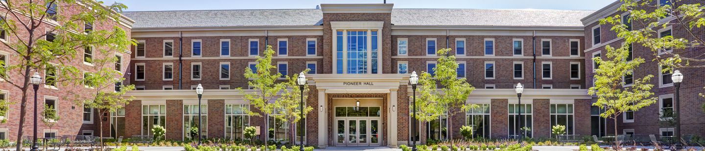 Front view of Pioneer Hall dormitory with greenery framing red brick and windows